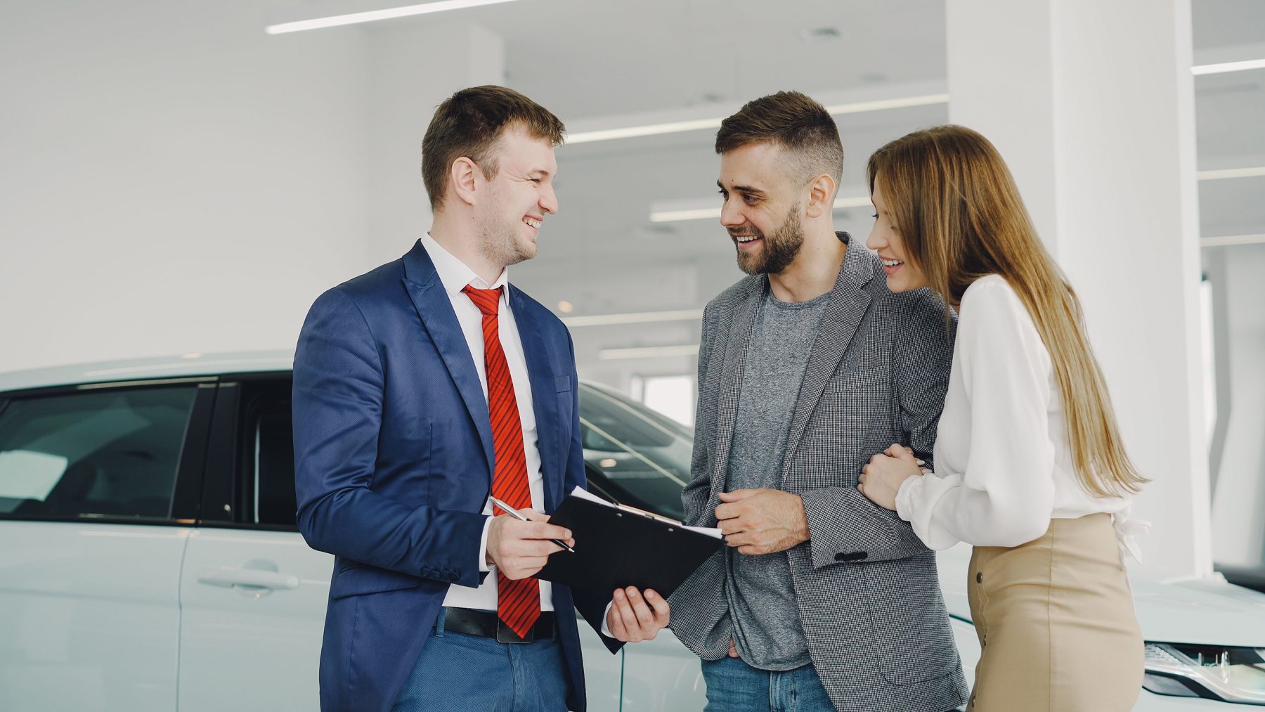 A salesman talking through the paperwork with a couple beside a white car