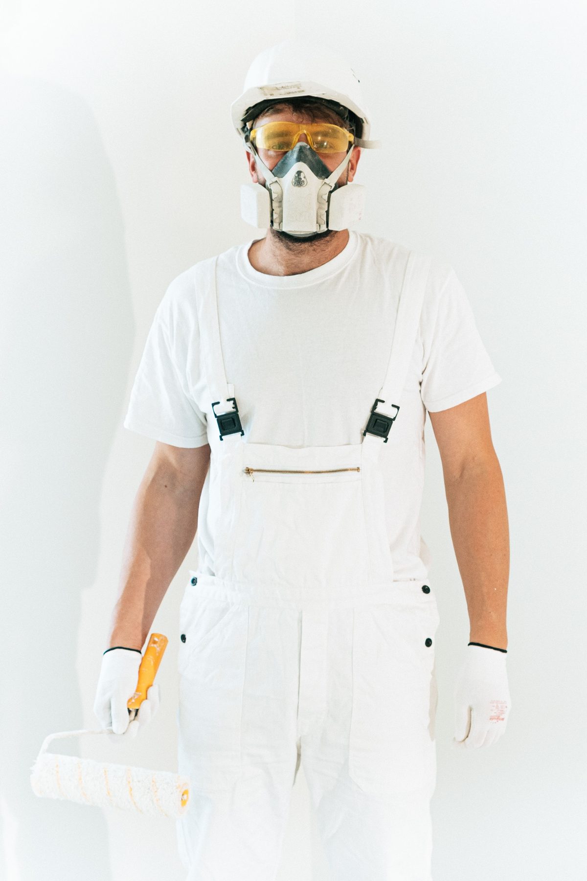 A cleaner in white overalls and gloves holding a paint-roller style mop, ready to start