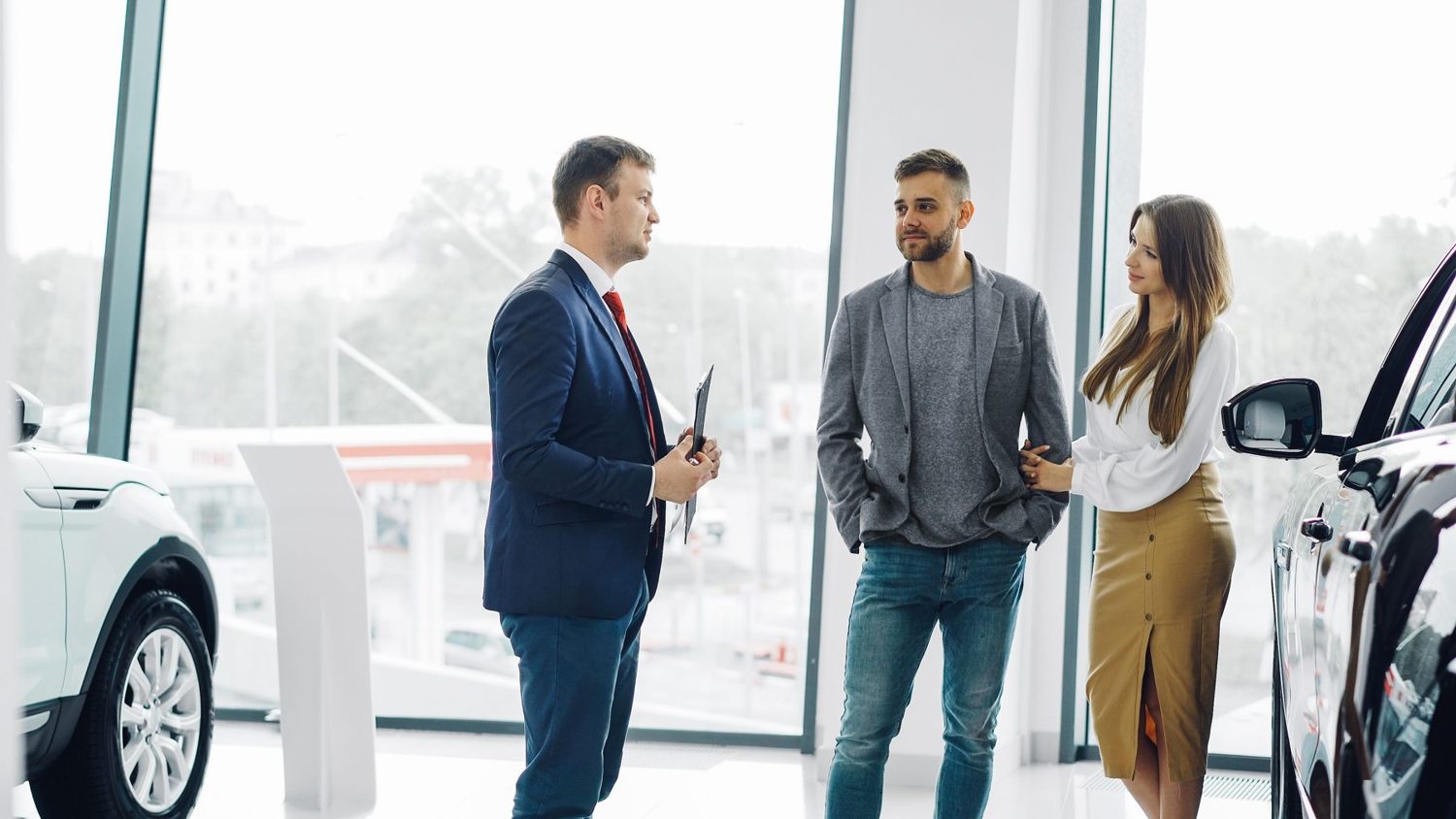 Three friendly people chatting in a bright showroom beside a car