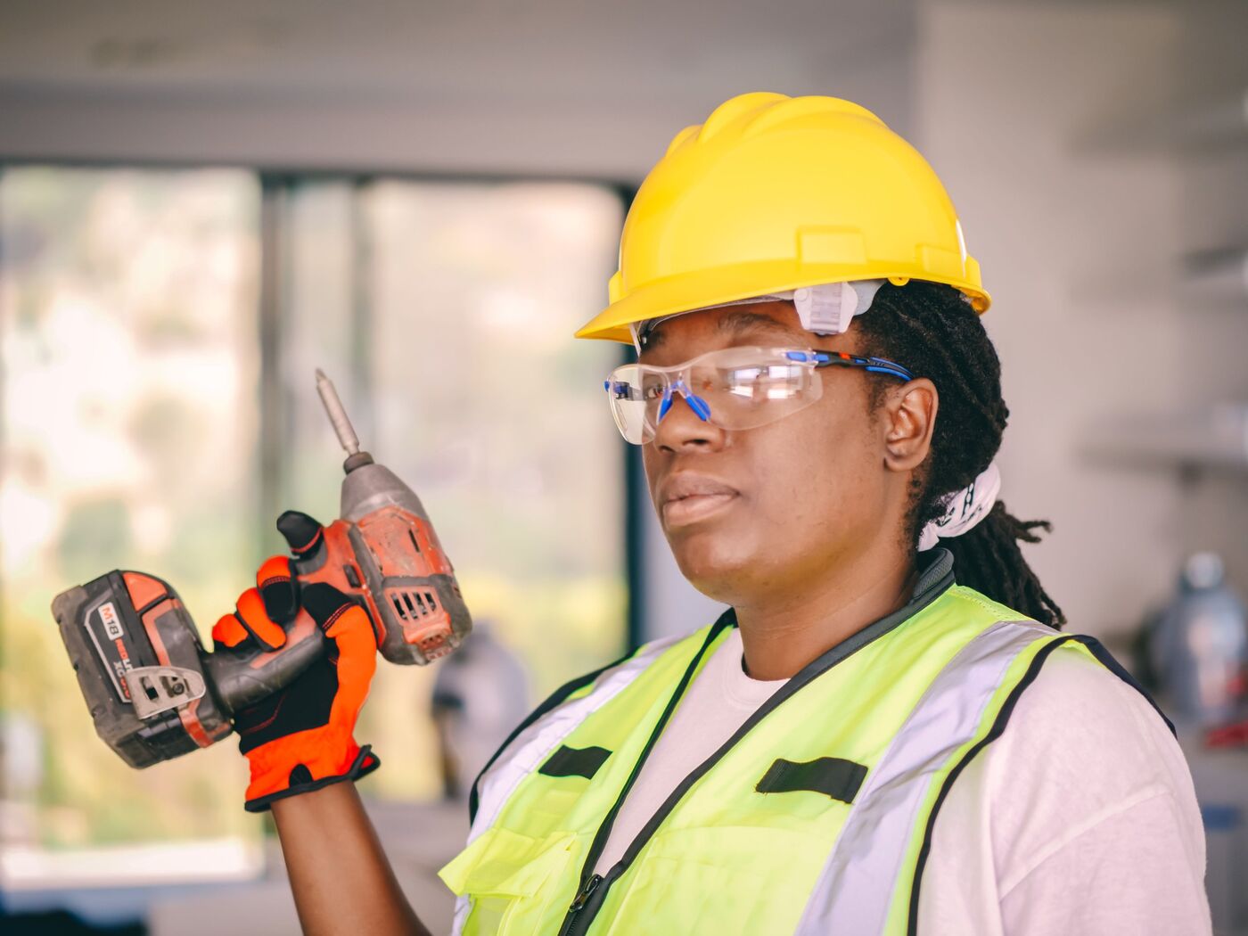 A smiling electrician in a yellow hard hat holding a power drill